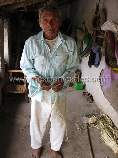 cozomatlan_nahua17.JPG - Palm weaving , this man is the last to wear the traditional Muslin peasant pants in the town. on the wall you can see the hammock hung up out of the way. Palm is on the floor both woven and ready to weave. These braids are sold to make hats .